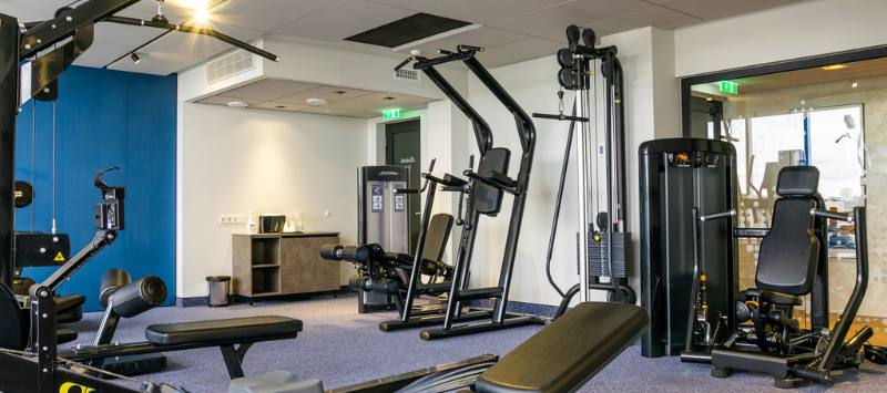 A picture of Nordic Hotel Forum's modern and bright gym. Various workout machines, a dumbbell area, and large windows are visible